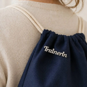 Pin "Trainerin" am Rucksack